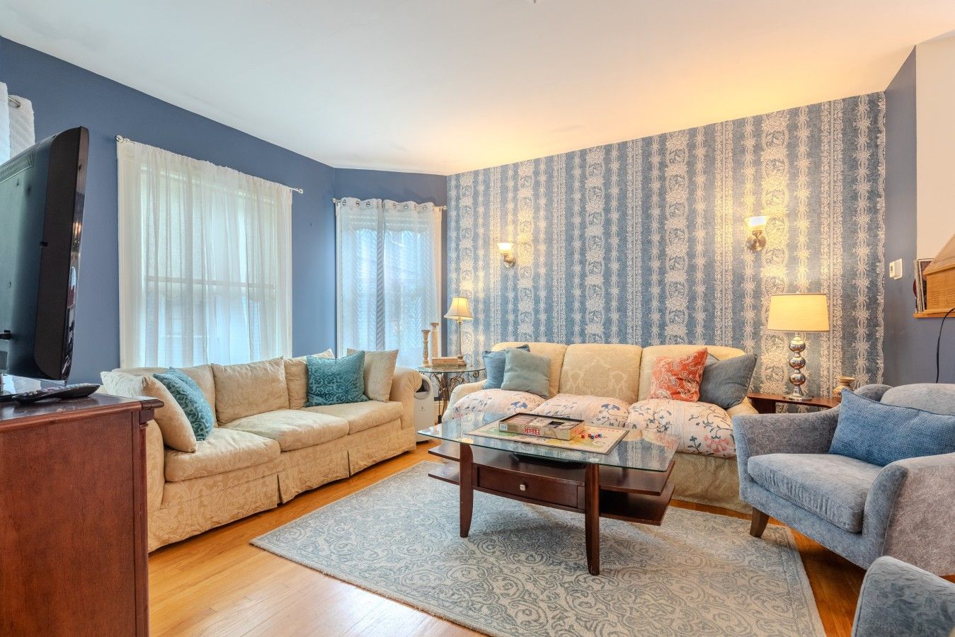 Un salon avec un canapé beige, un fauteuil bleu, une table basse et un téléviseur.