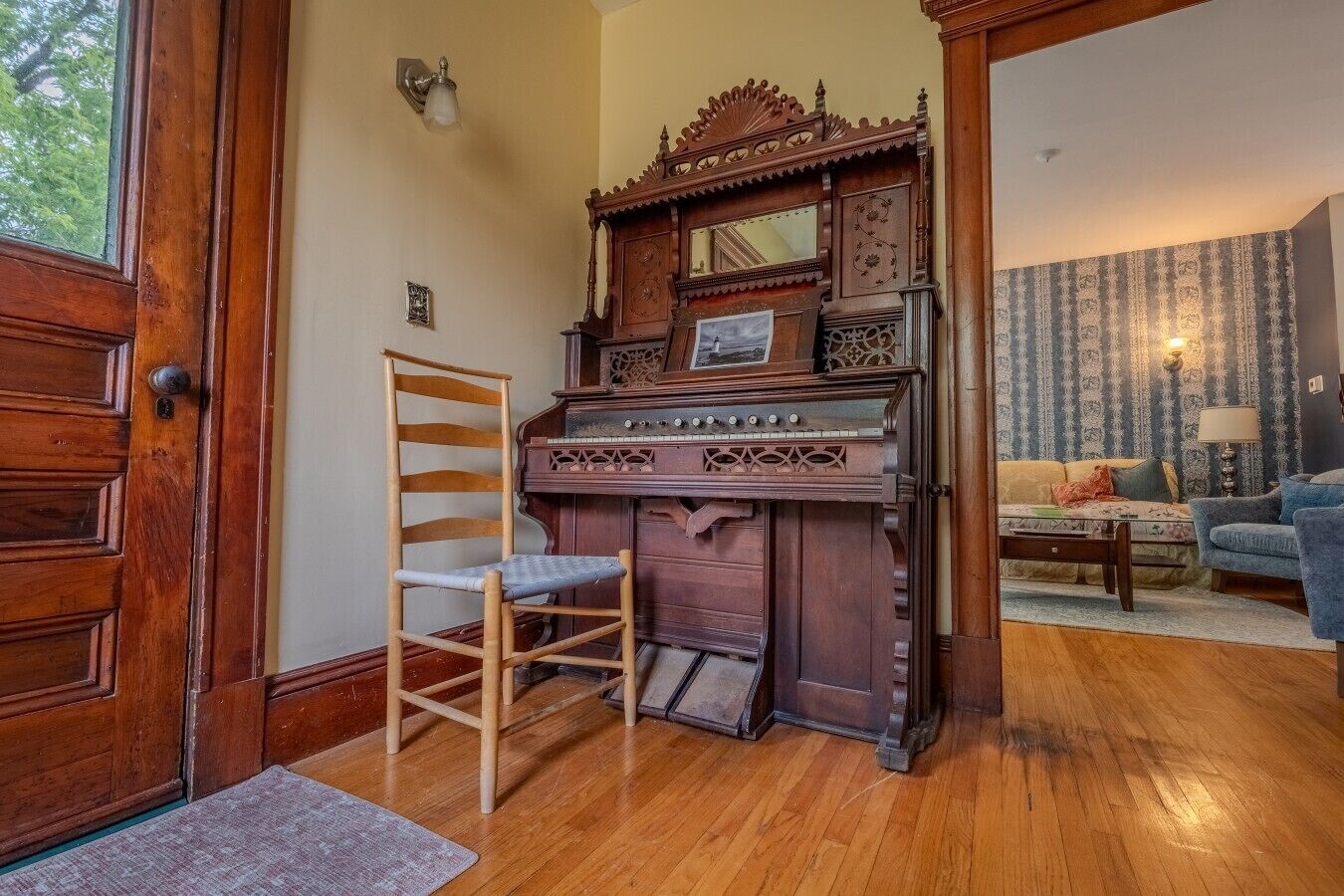 Een kamer met een houten piano, een houten stoel, een bank en een lamp.