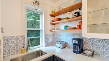 A kitchen with a window, a sink, a toaster, a coffee maker, and shelves with dishes and glasses.