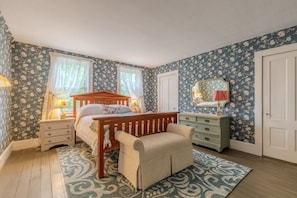 A bedroom with a wooden bed, a bench, a dresser, and a mirror.