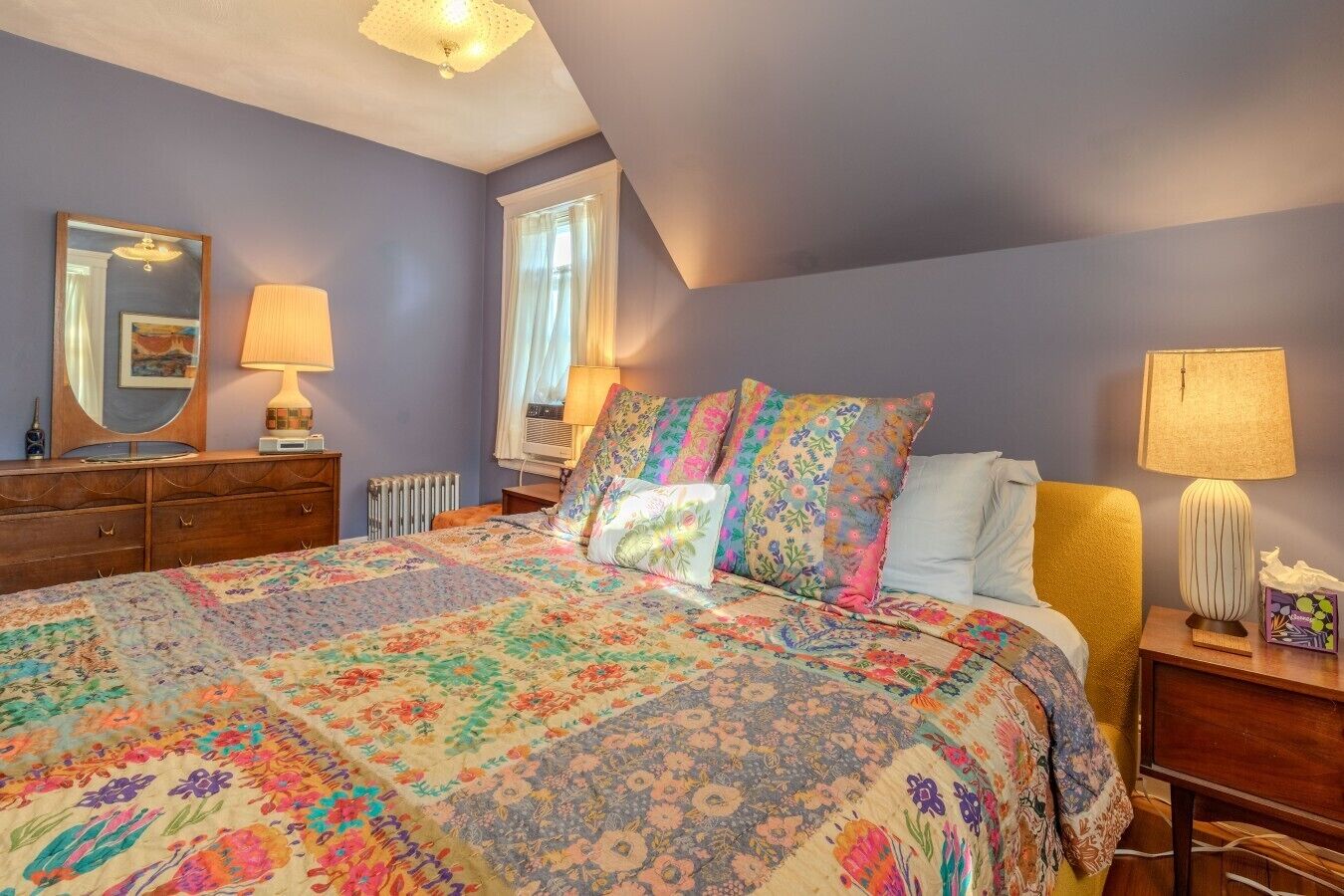 A bedroom with a large bed, a dresser, a mirror, and a window with curtains.