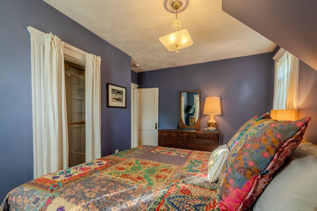 A bedroom with a bed, dresser, and a ceiling light fixture.