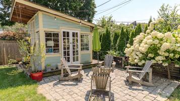 A small wooden structure with a porch, outdoor seating, and a garden with white flowers.