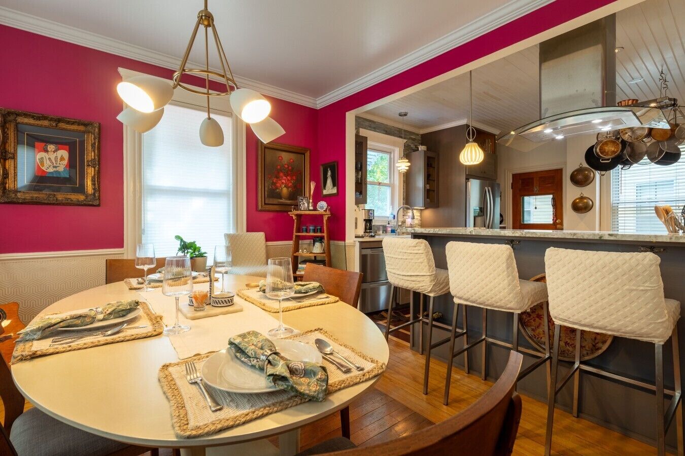 A dining area with a round table set for four, a kitchen in the background, and a bar area with stools.
