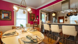 Uma área de refeições com uma mesa redonda posta para quatro pessoas, cozinha ao fundo e um bar com banquetas.