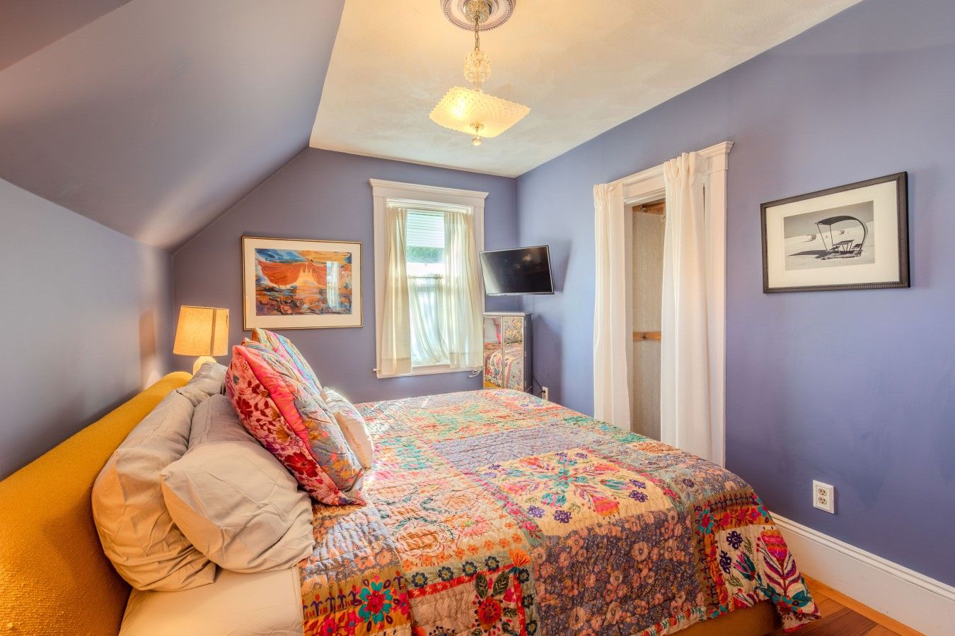 Un dormitorio con cama, ventana, televisor y obras de arte en las paredes.