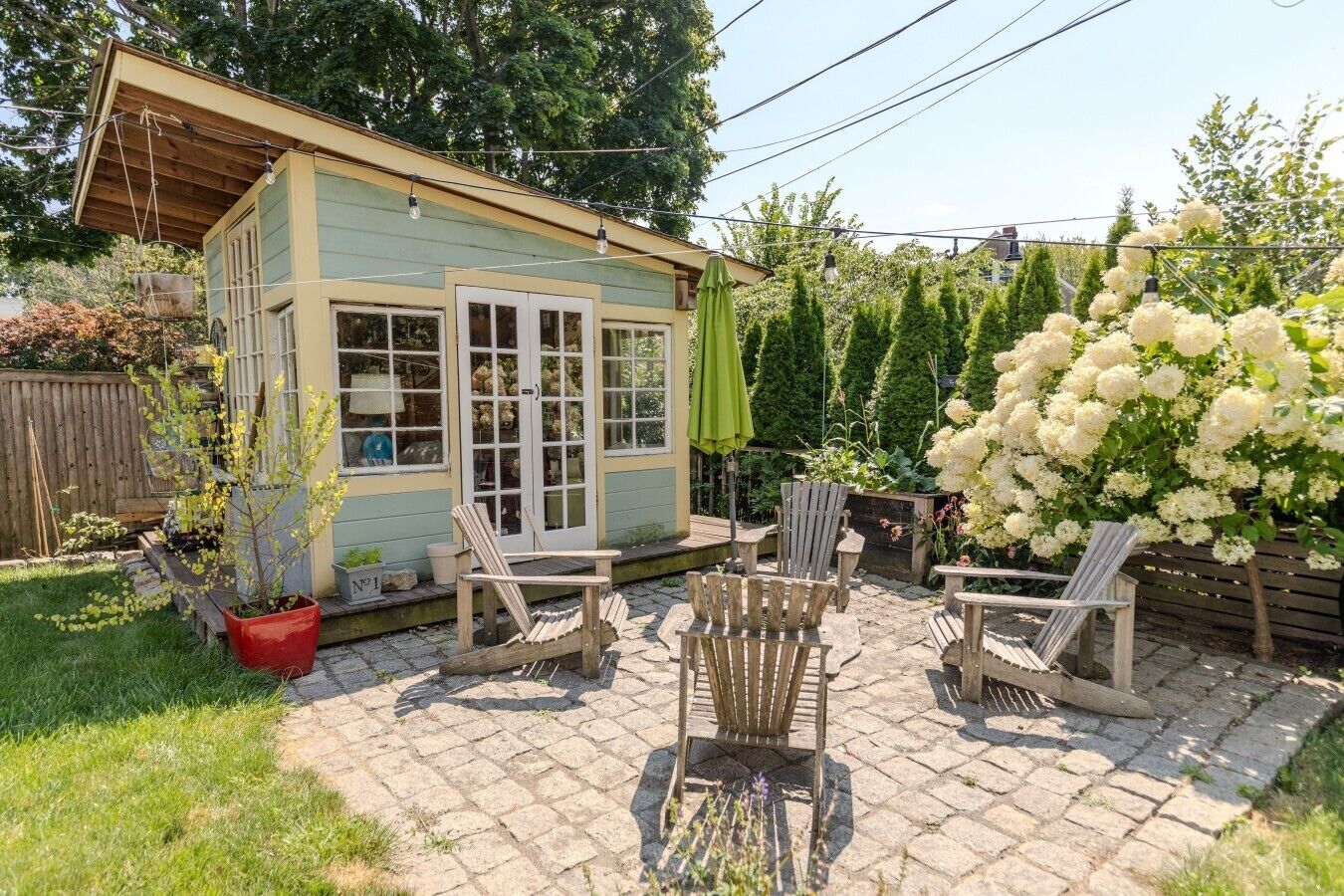 A small wooden structure with a porch, outdoor seating, and a garden with white flowers.