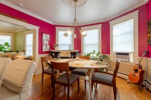 Comedor con una mesa dispuesta para cuatro personas, rodeada de sillas, en una habitación con paredes rosadas y piso de madera.