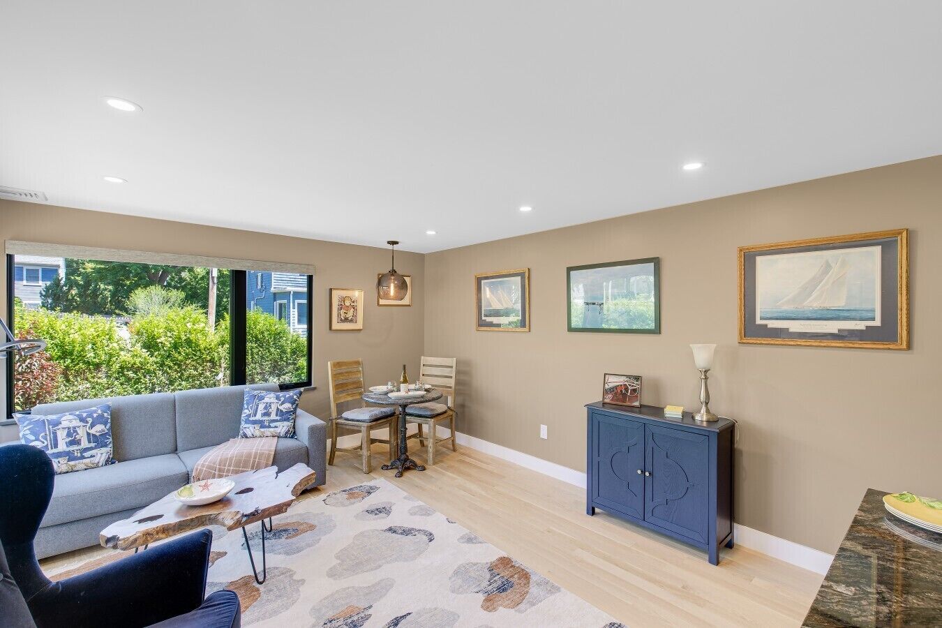 A living room with a sofa, dining table, chairs, and a cabinet. There are framed pictures on the wall.