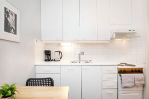 Ett kompakt kök med vita skåp, en kaffebryggare, en vattenkokare, ett handfat och en spis.