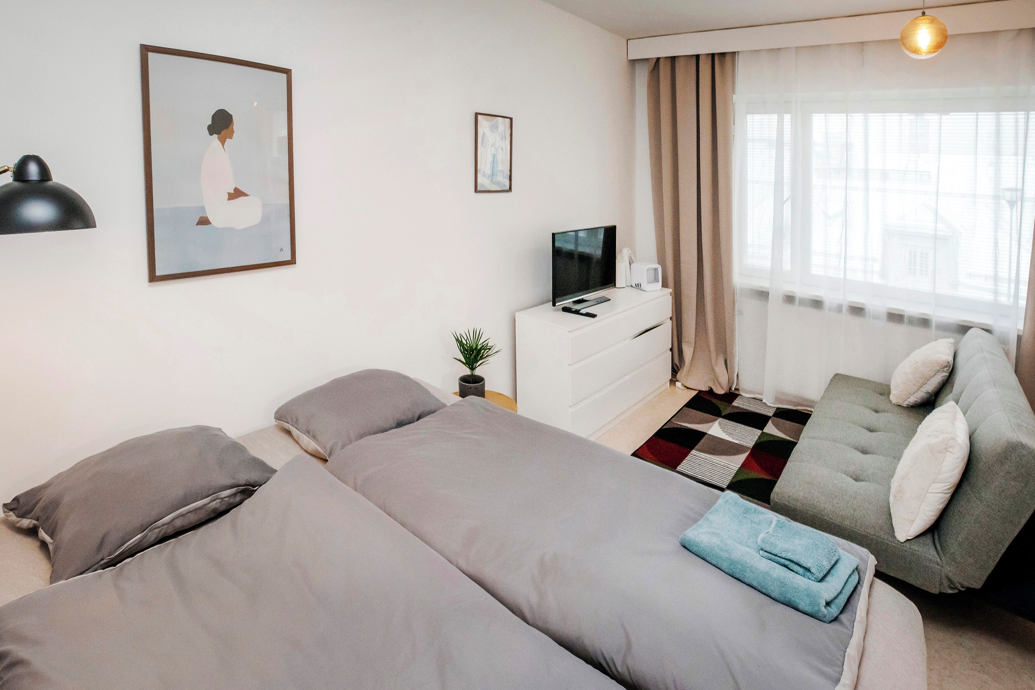 Hotellihuone, jossa on kaksi sänkyä, televisio, työpöytä ja ikkuna, jossa on verhot.