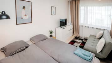 Hotellihuone, jossa on kaksi sänkyä, televisio, työpöytä ja ikkuna, jossa on verhot.