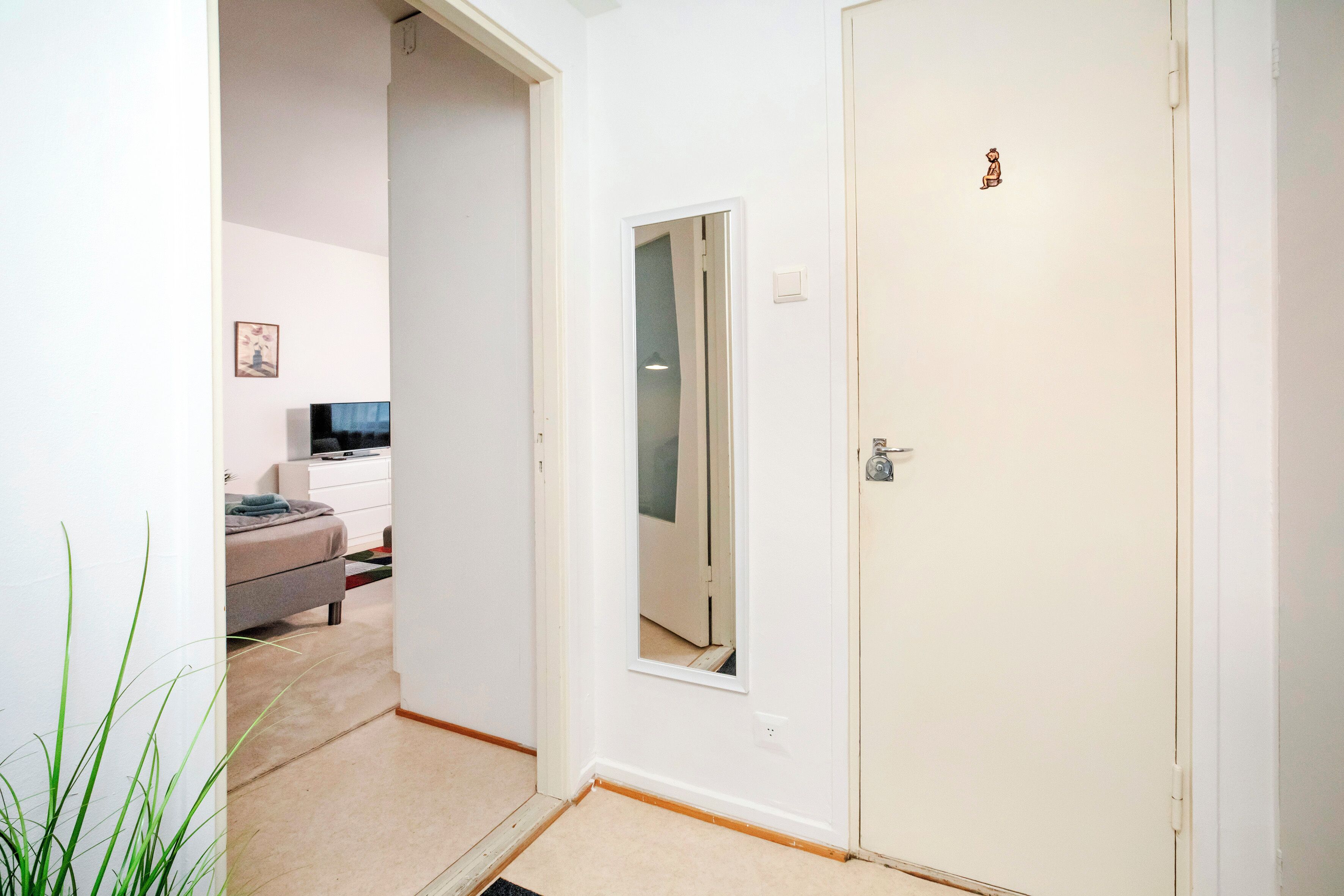 A hallway with a bed, a dresser, and a television in a room.