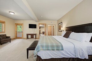 A bedroom with a bed, a bench, a television, and a door leading to another room.