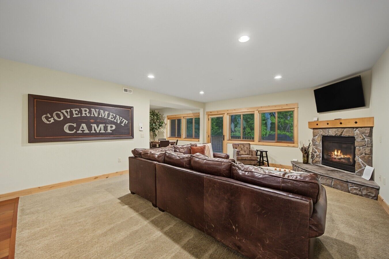 A living room with a large brown leather sofa, a stone fireplace, and a sign that reads 'GOVERNMENT CAMP'.