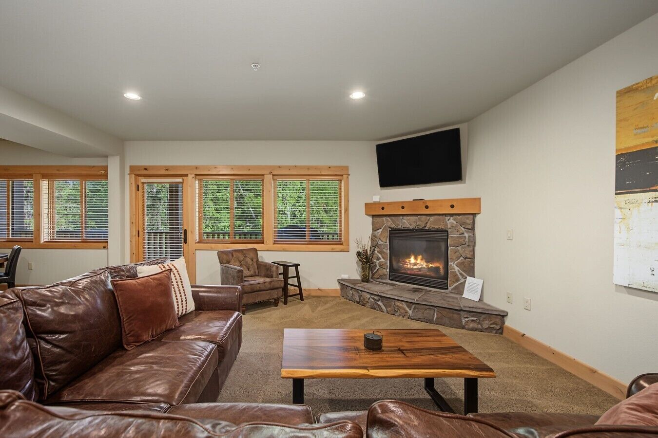 A living room with a stone fireplace, leather furniture, and large windows with blinds.