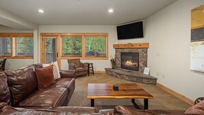 Ein Wohnzimmer mit Kamin aus Stein, Ledermöbeln und großen Fenstern mit Jalousien.