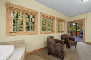 A bathroom with a bathtub, three wooden-framed windows, and two upholstered chairs.