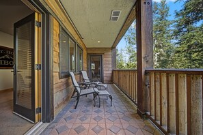 Ein überdachter Außenbereich mit Holzterrasse, zwei Stühlen und einer Glastür, die zu einem Raum führt.