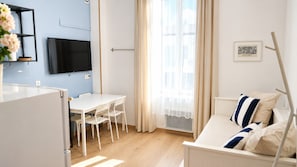 A modern living room with a white sofa, a dining table with chairs, a flat-screen TV mounted on the wall, and a window with curtains. - Cosy Entire Apartment up to 4 guests - with free parking - 1 Min from Monaco (Beausoleil)