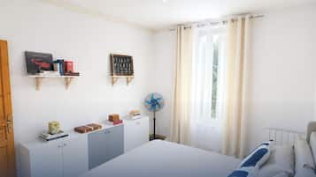 A bedroom with a bed, a bedside table, a fan, and a window with curtains.