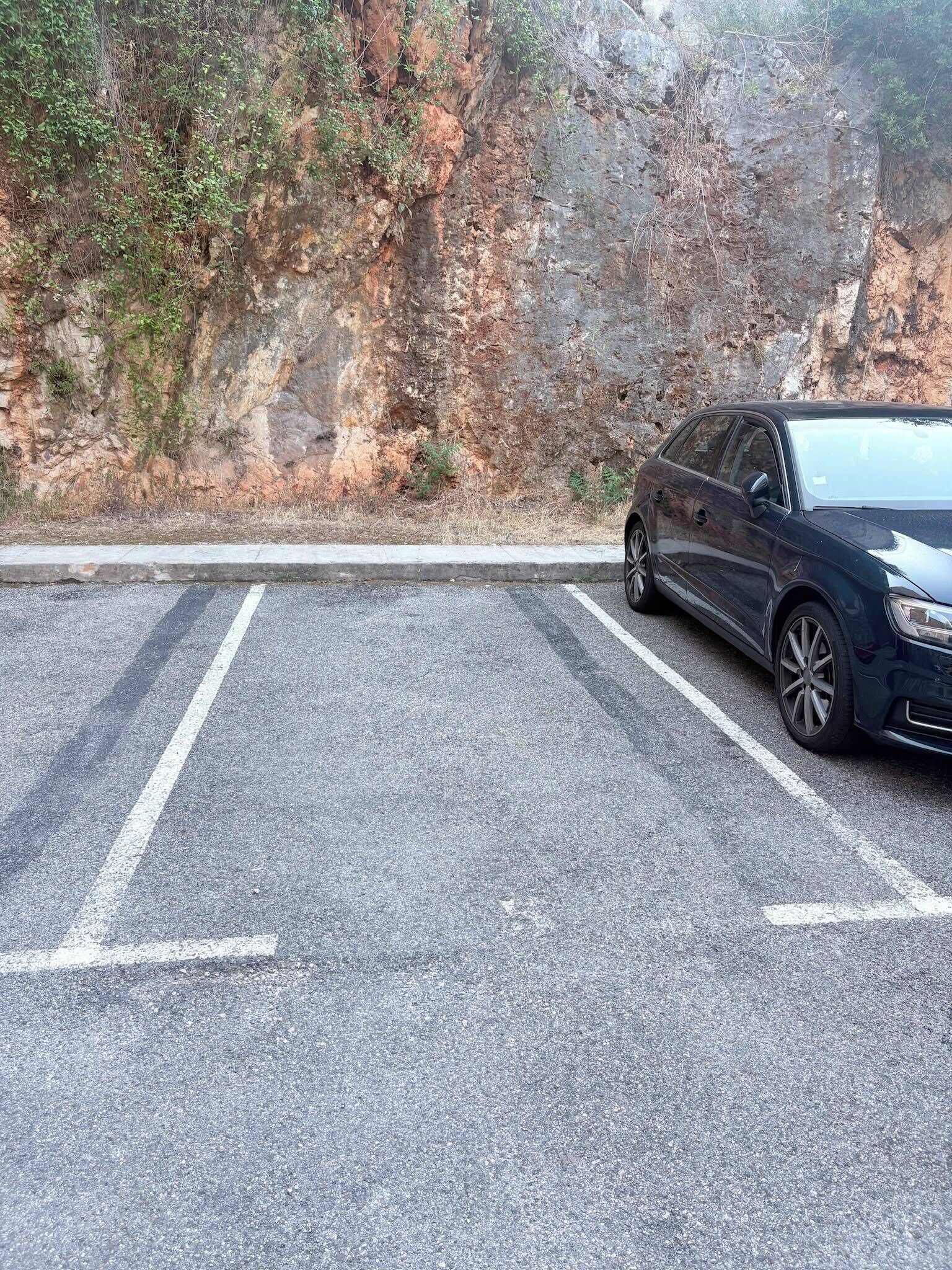 A parking area with a car parked on the right side, adjacent to a rocky cliff.
