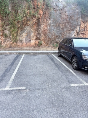 Un espace de stationnement où une voiture est garée sur le côté droit, à côté d’une falaise rocheuse.