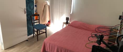 A bedroom with a bed, a chair, a small table, a curtain, and a wall with a patterned design.