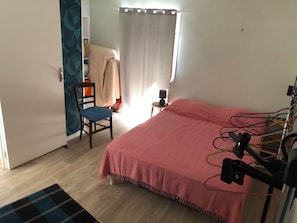A bedroom with a bed, a chair, a small table, a curtain, and a wall with a patterned design. - DETACHED HOUSE WITH ACCESS TO A POND FOR FISHERS (Bussière Galant)
