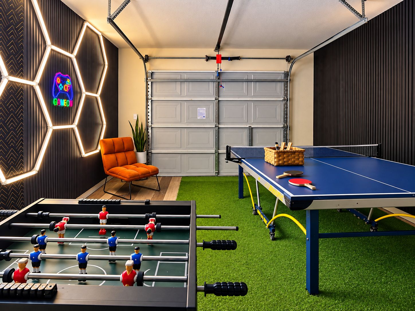Um quarto com mesa de pebolim, mesa de pingue-pongue e um letreiro neon.