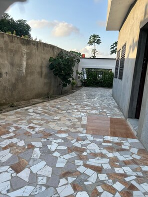 A courtyard with a tiled floor, a concrete wall, and a building with a gate. - Romantic villa @ Baie Des Milliadaires Abidjan-CI not far from Romano Lodge. (Abidjan)
