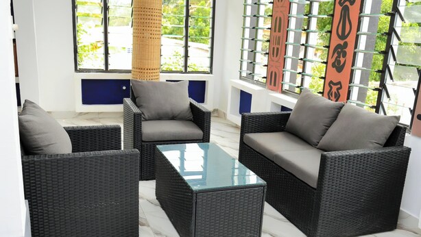 Une pièce meublée avec des meubles en osier, notamment un canapé et deux fauteuils, ainsi qu’une table basse avec un plateau en verre.