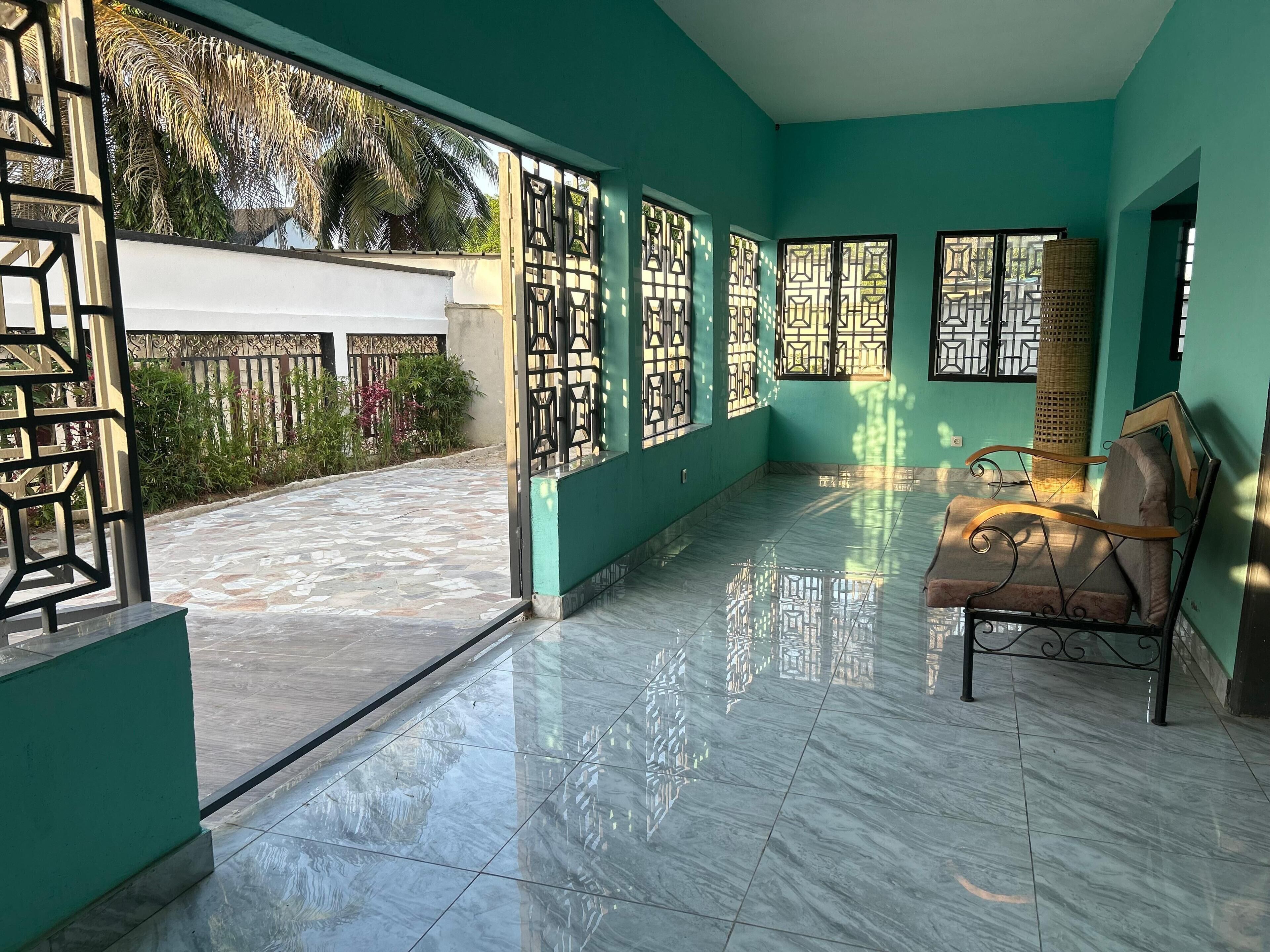 A spacious room with a tiled floor, a bed with a headboard, and a window with a decorative grille.