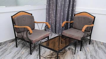 Two chairs with wooden armrests and a glass table in a room with marble flooring.