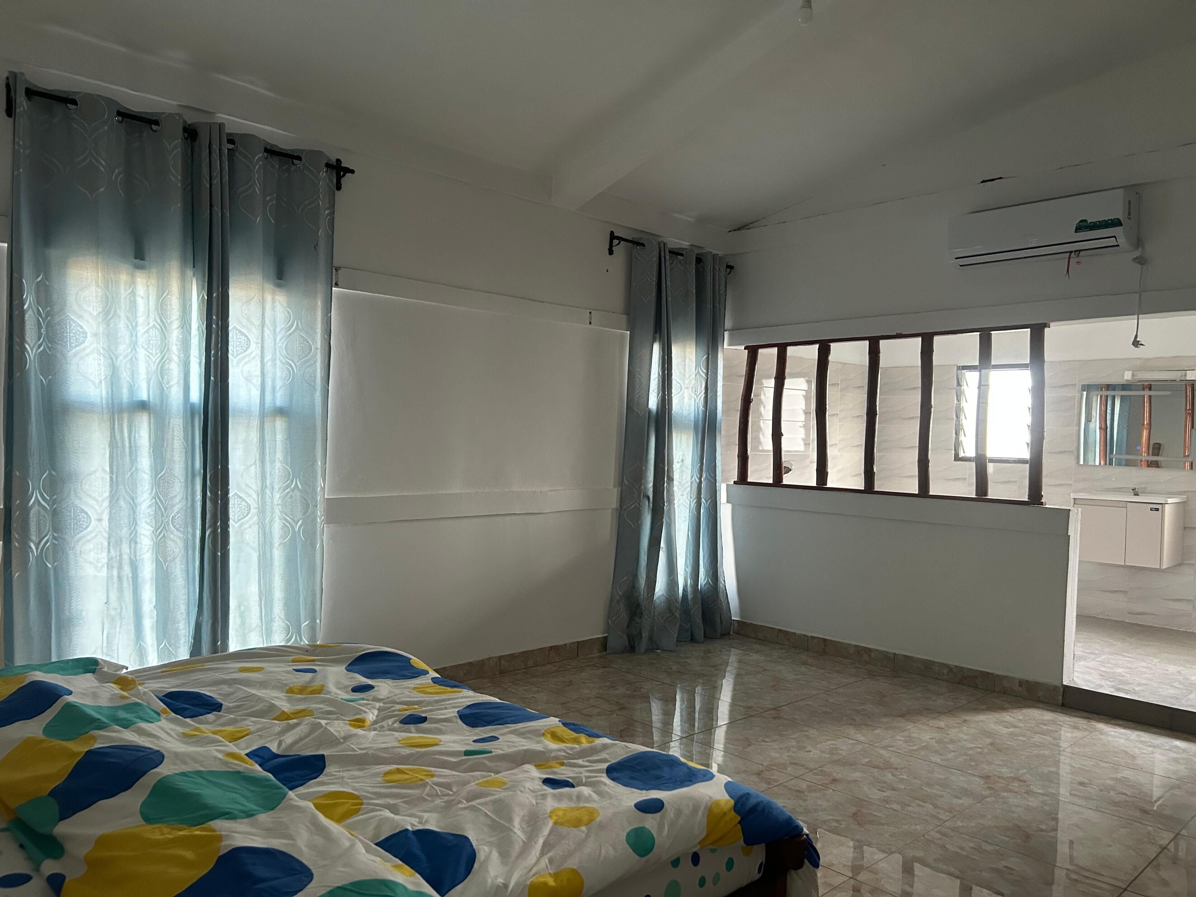 Et hotelværelse med en seng, et vindue med tremmer, et badeværelse med et spejl og en aircondition.