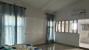 Une chambre d’hôtel avec un lit, une fenêtre avec des barreaux, une salle de bain avec un miroir et un appareil de climatisation.