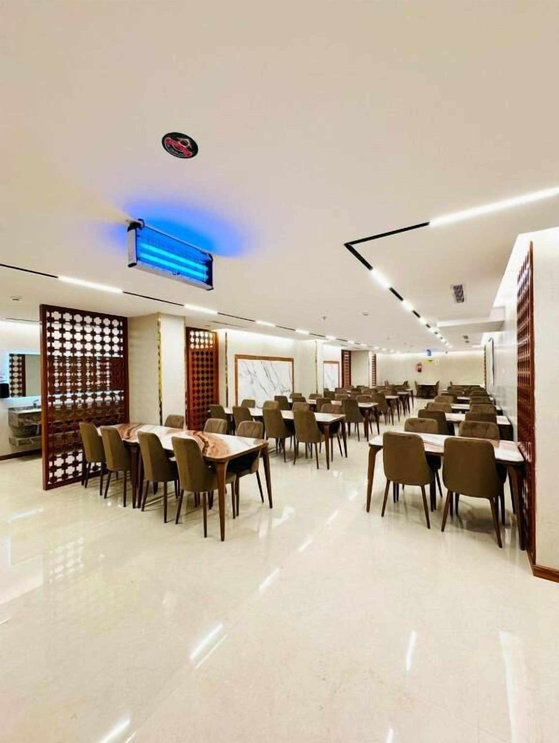 Un comedor amplio con varias mesas y sillas, un techo con iluminación empotrada y un separador decorativo.