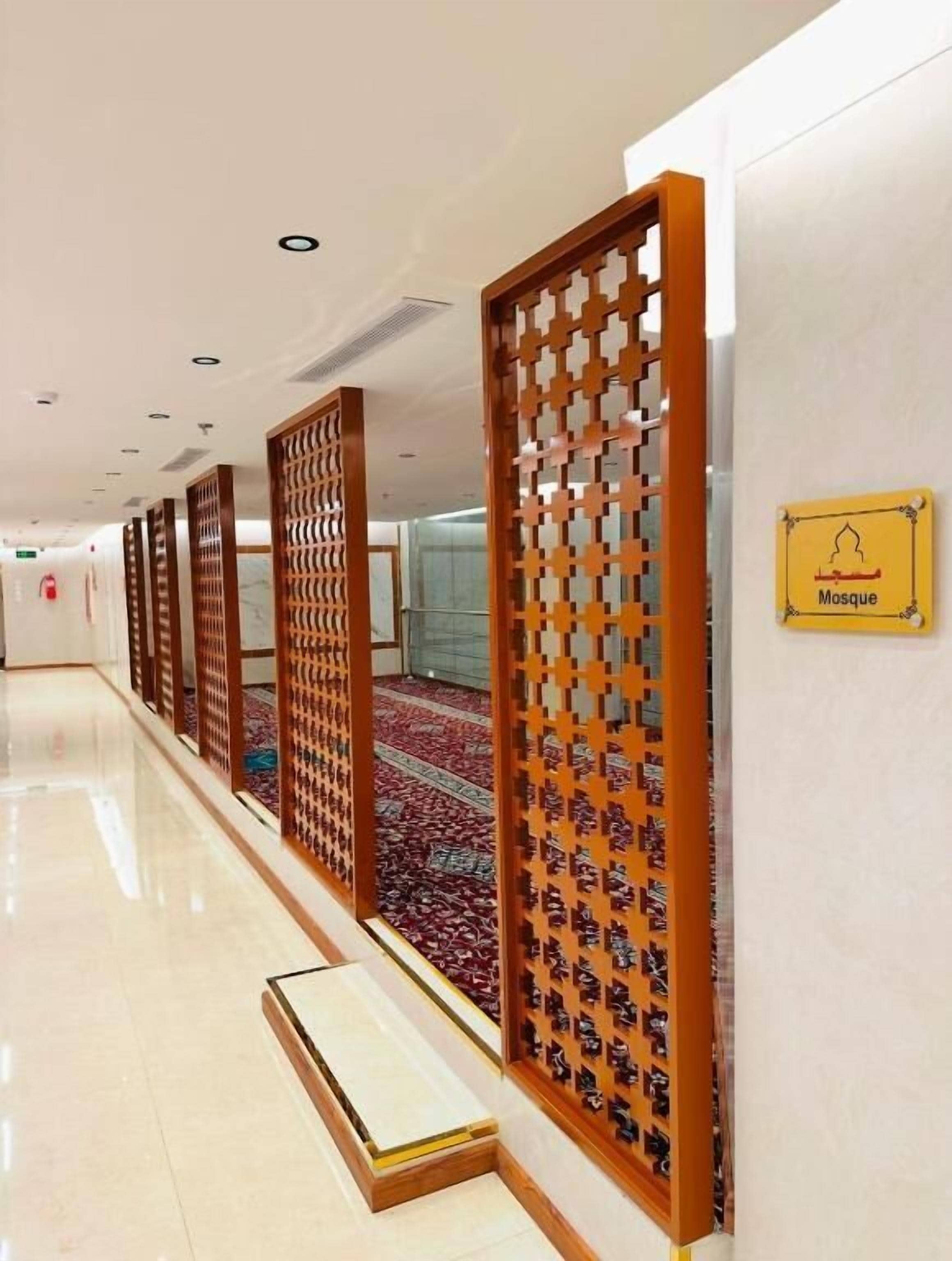 Un pasillo con separaciones de madera que conduce a una mezquita, un cartel indicando la ubicación y un suelo alfombrado.