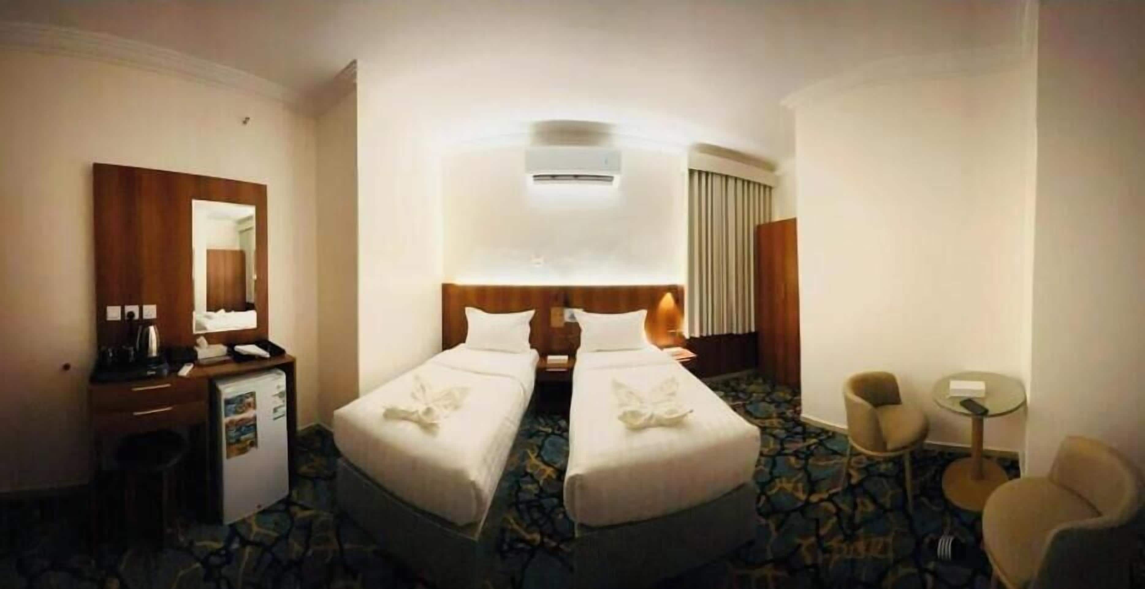 A hotel room with two beds, a desk with a chair, a small table, and a mirror.