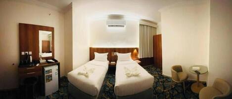 A hotel room with two beds, a desk with a chair, a small table, and a mirror.