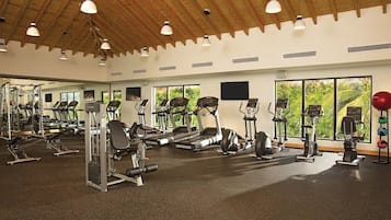 Une salle de sport équipée de divers appareils d’exercice, dotée de grandes fenêtres et d’un plafond en bois.