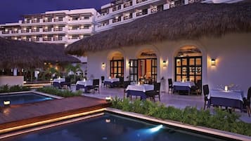 Un hotel con varias opciones de restauración, una piscina y un edificio con techo de paja.