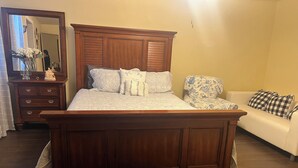 A bedroom with a wooden bed, a dresser, a mirror, a sofa, and a floral-patterned chair. - Your Ideal Stay Near the Stockyards (Fort Worth)