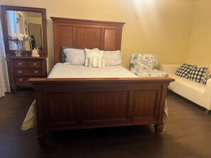 A bedroom with a wooden bed, a dresser, a mirror, a sofa, and a floral-patterned chair. - Your Ideal Stay Near the Stockyards (Fort Worth)