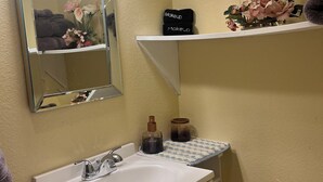 A bathroom with a white sink, a mirror, and two shelves with toiletries. - Your Ideal Stay Near the Stockyards (Fort Worth)