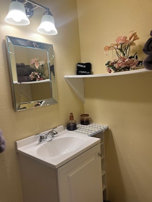 A bathroom with a white sink, a mirror, and two shelves with toiletries. - Your Ideal Stay Near the Stockyards (Fort Worth)
