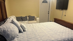 A bedroom with a large bed, a bedside table, a chair, a television mounted on the wall, and a door. - Your Ideal Stay Near the Stockyards (Fort Worth)