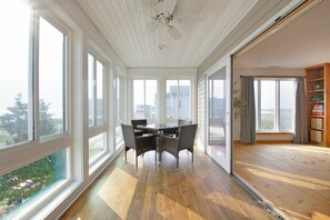 Ein sonnendurchflutetes Zimmer mit Esstisch und Stühlen, großen Fenstern und Blick ins Freie.