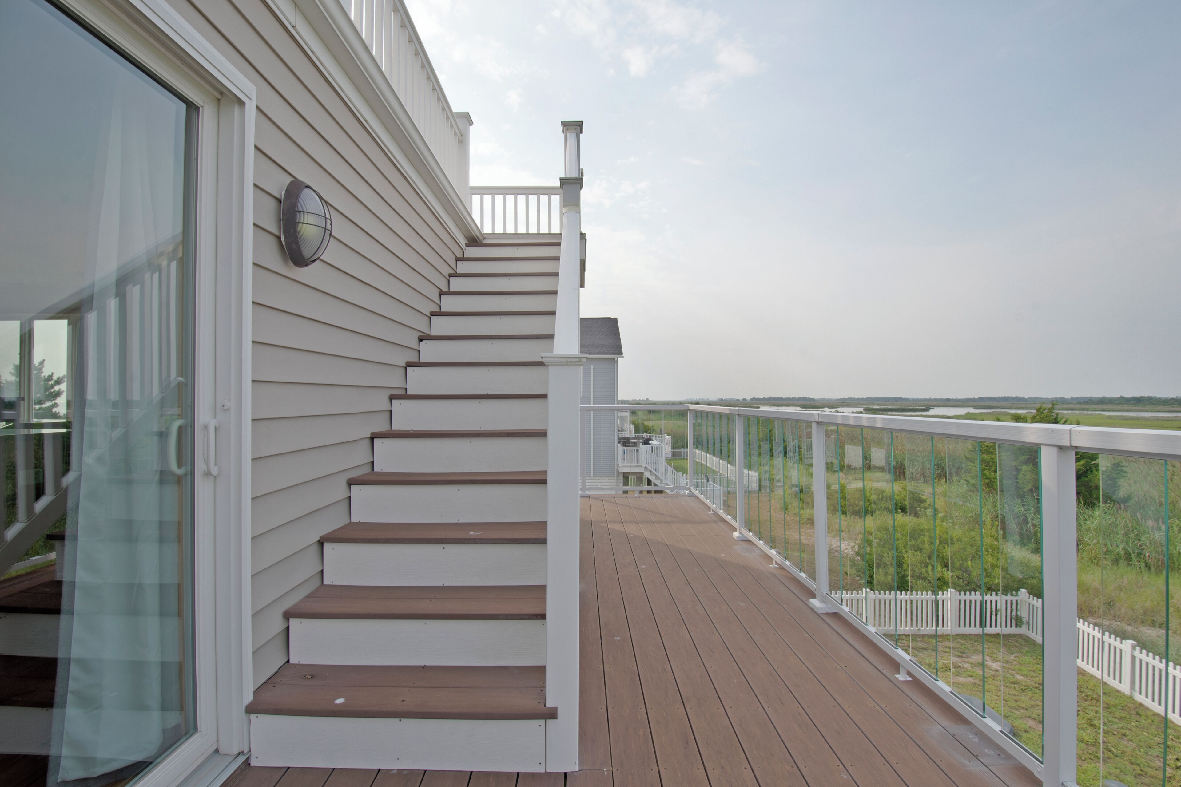 A wooden deck with a white railing and a glass door leading to a room.