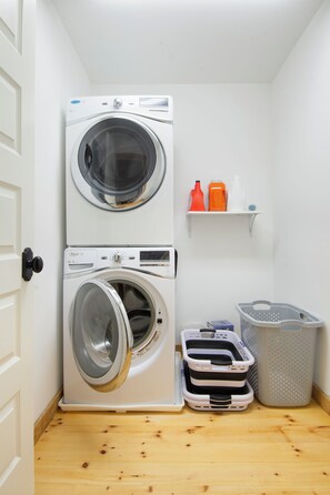 A laundry room with two stacked washing machines, a shelf with cleaning supplies, and laundry baskets. - Private, serene house 5-min to beach with panoramic views from two decks (Milford)